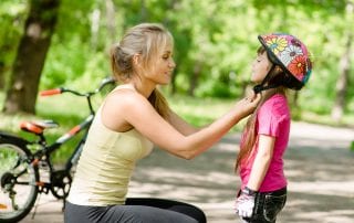 young mother adjusts daughter bicycle helmet